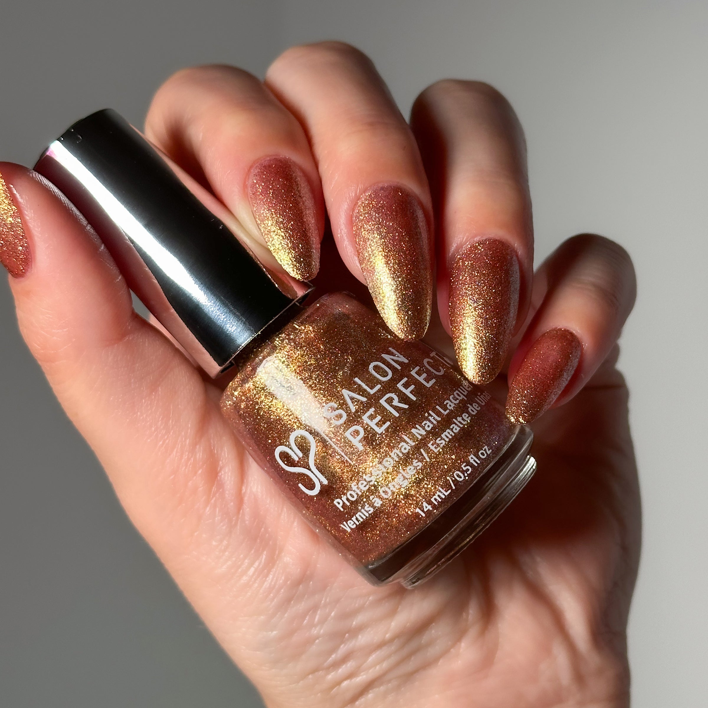 Close-up of a model's hand wearing Salon Perfect Flash Nail Lacquer .5oz 435 Bling It On holding the nail polish bottle.