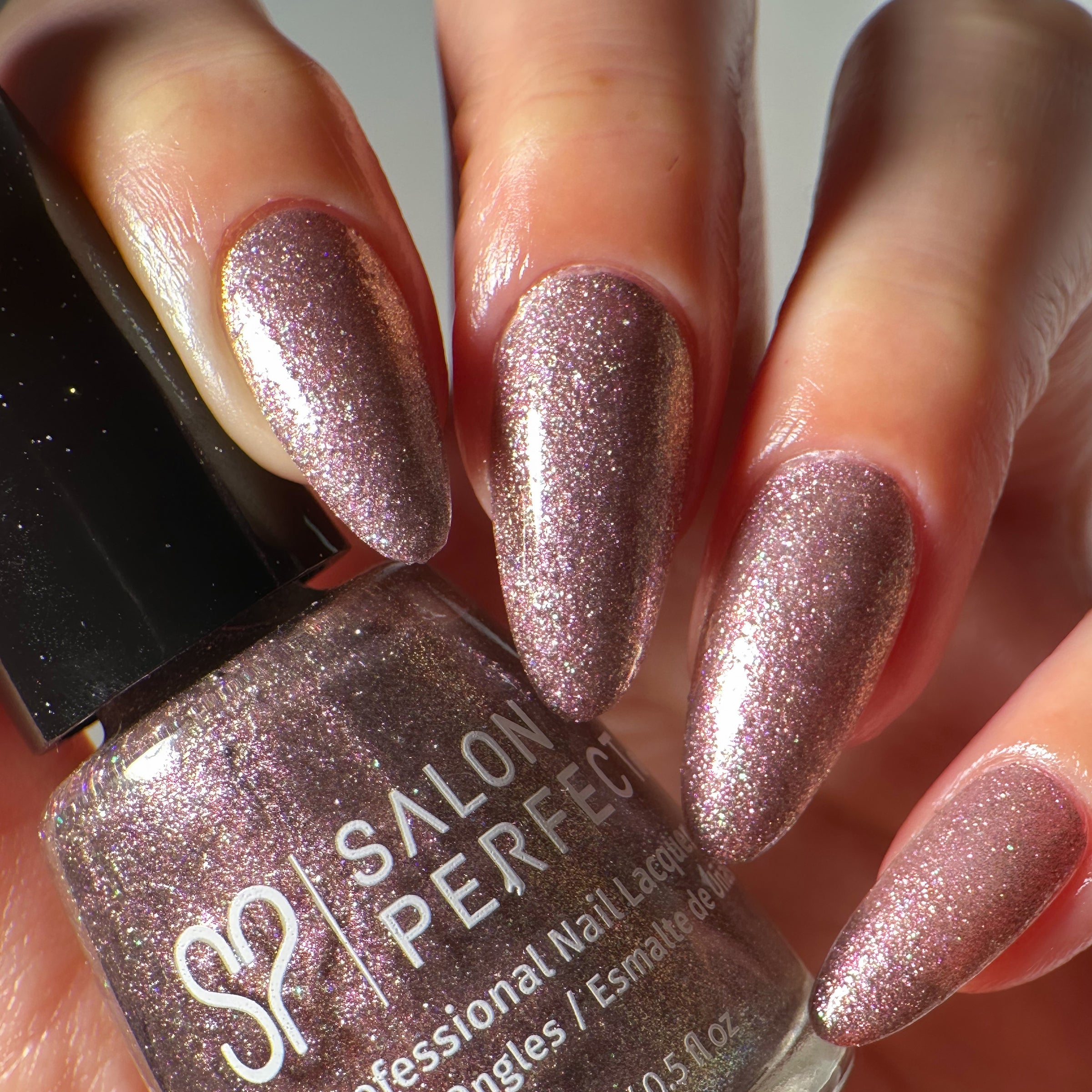 Close-up of a model's hand wearing Salon Perfect Flash Nail Lacquer .5oz Gliterally Obsessed holding the nail polish bottle.