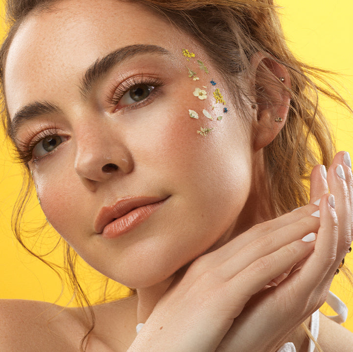 Woman with bright floral-inspired face paint in spring colors on a yellow background