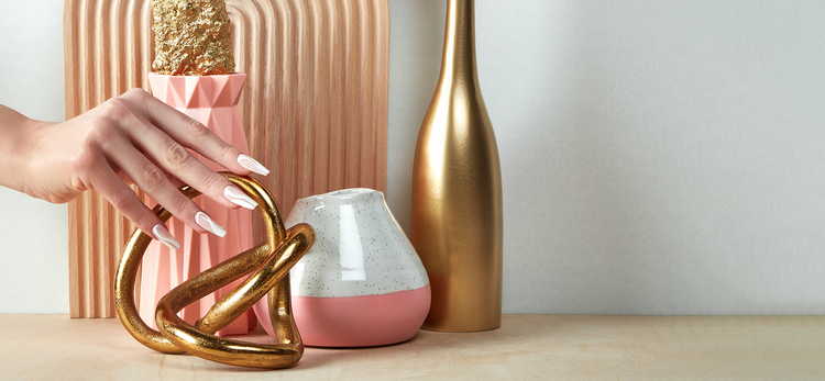 Decorative gold sculpture on a table with a pink vase and white container in the background.