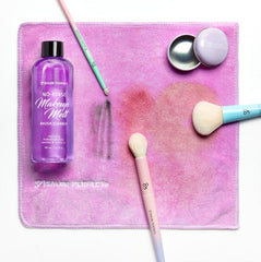 Makeup brush cleaner bottle with brushes and a towel on a pink background
